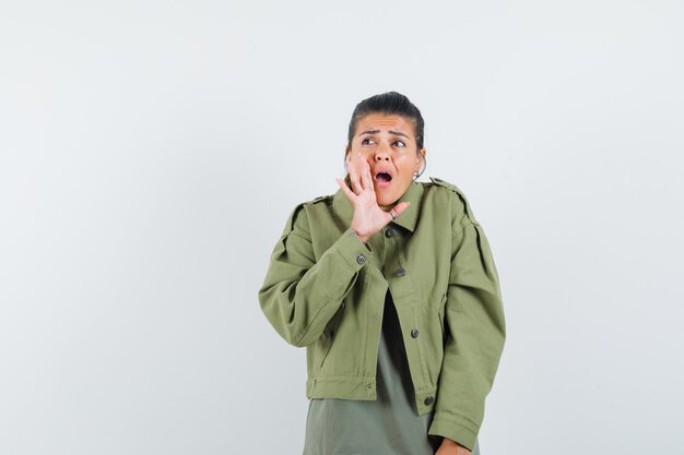 woman in jacket, t-shirt holding hand near open mouth and looking surprised