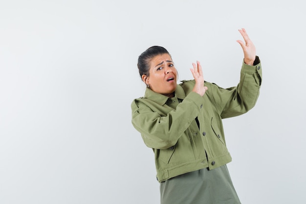 woman in jacket, t-shirt holding hands to defend herself and looking scared