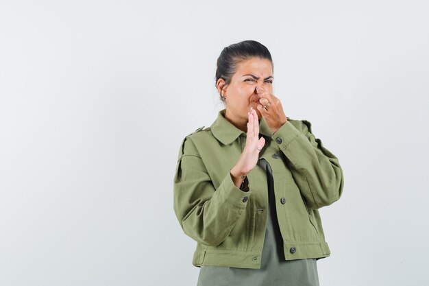 woman in jacket, t-shirt pinching nose due to bad smell and looking disgusted