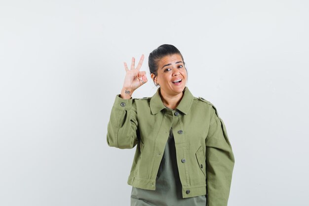 Woman in jacket, t-shirt showing ok gesture and looking merry