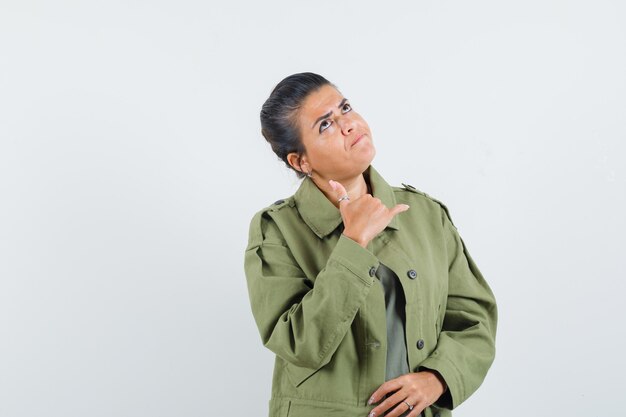 Woman in jacket, t-shirt showing phone gesture and looking pensive