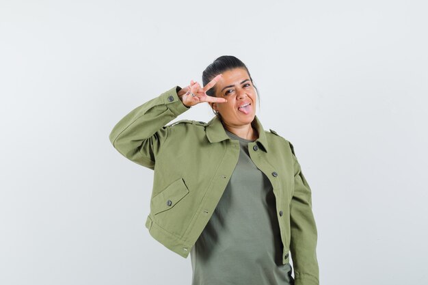 woman in jacket, t-shirt showing V-sign near eye and looking happy