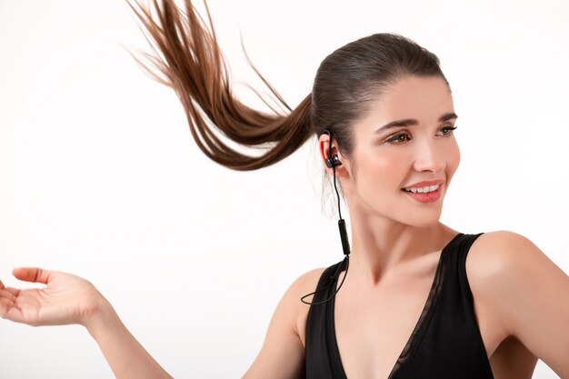 woman in jogging black top listening to music on earphones posing isolated on white