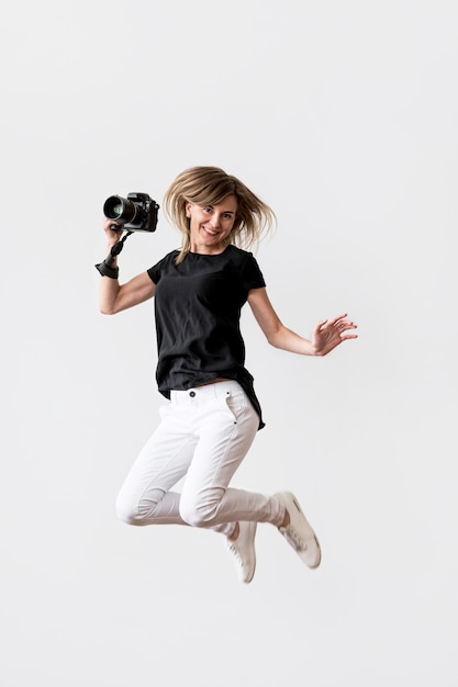 Free photo woman jumping and holding a camera