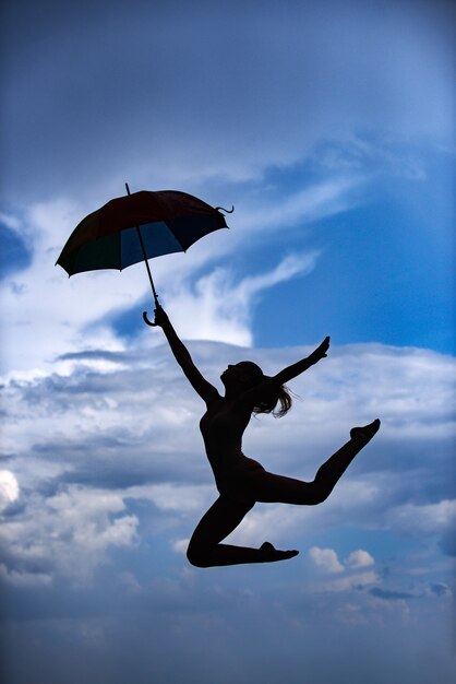 Woman jumping with umbrella ballet dancer isolated on sky background expressive artistic dance conce...