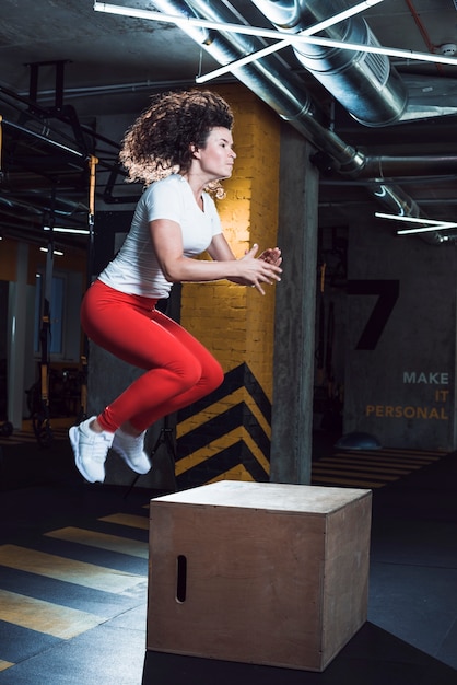 Woman jumping on wooden box in fitness club