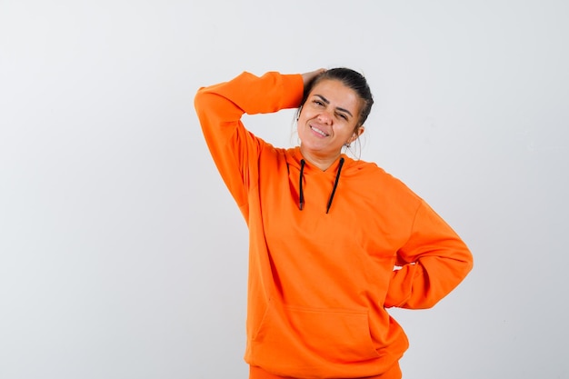 woman keeping hand on head in orange hoodie and looking charming
