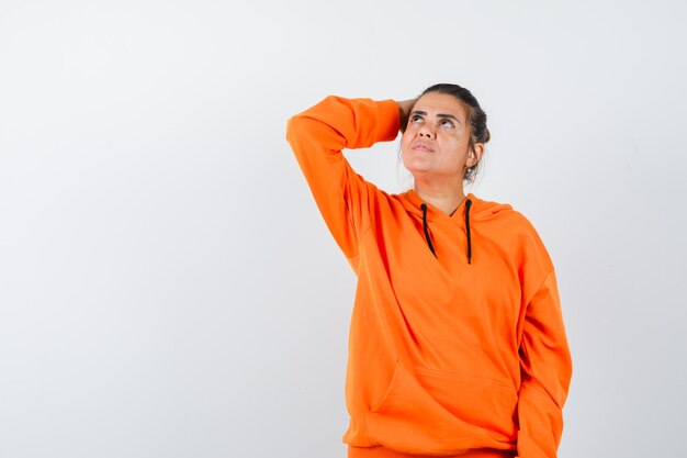 woman keeping hand on head in orange hoodie and looking dreamy