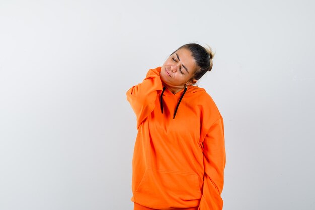 Woman keeping hand on neck in orange hoodie and looking tired