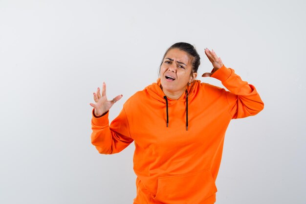 Woman keeping hands in puzzled gesture in orange hoodie