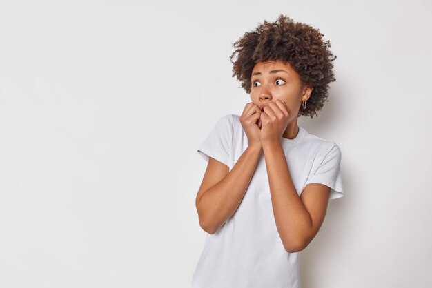 woman keeps hands on mouth stares bugged eyes away trembles from fear wears casual t shirt isolated on white blank copy space for your advertising content