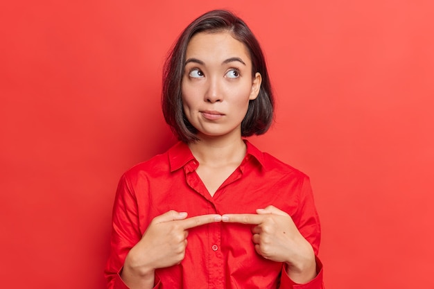  woman keeps index finger opposite feels doubtful wears shirt focused above poses on red 