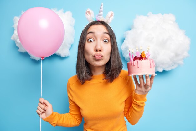 여자는 접힌 입술을 유지하고 휴일 이벤트가 맛있는 케이크를 보유하고 팽창 된 풍선이 26 번째 생일을 축하합니다.