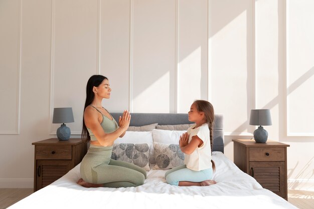 Woman and kid meditating in bed full shot