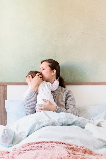 Женщина целует ребенка на руках в постели