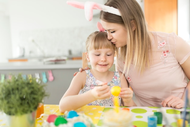Woman kissing daughter painting eggs