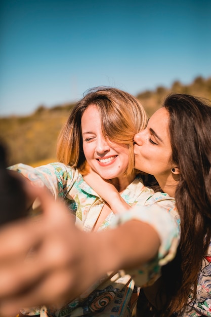 Woman kissing friend and taking selfie