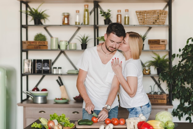 Free photo woman kissing her boyfriend cutting red tomato with knife