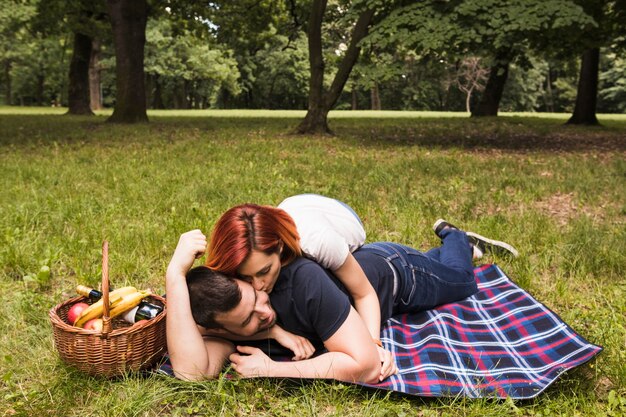 Woman kissing her boyfriend lying on blanket over green grass in the park