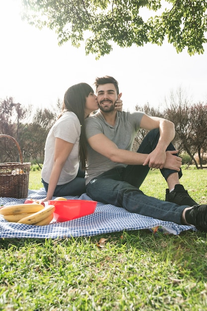 Женщина целует своего парня, сидящего на одеяле в парке