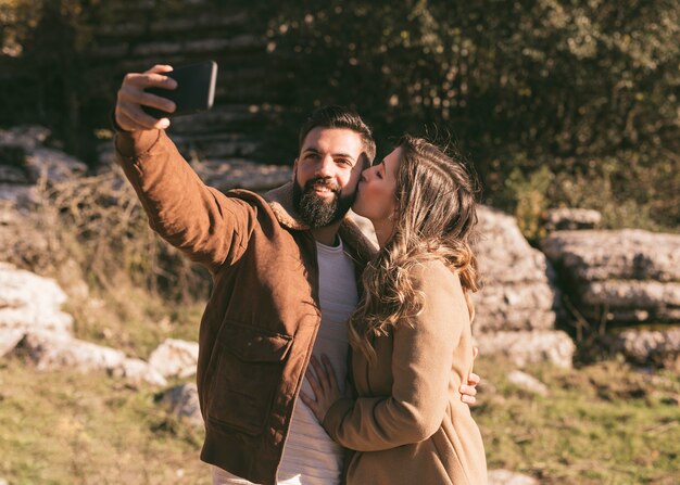 Woman kissing her boyfriend while he takes a selfie