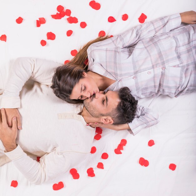バラの花びらが付いているベッドの上の男にキスをする女性