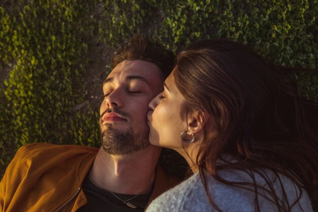 Женщина целует мужчину в щеку лежа на траве