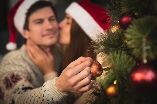 Woman kissing man decorating christmas tree with globes