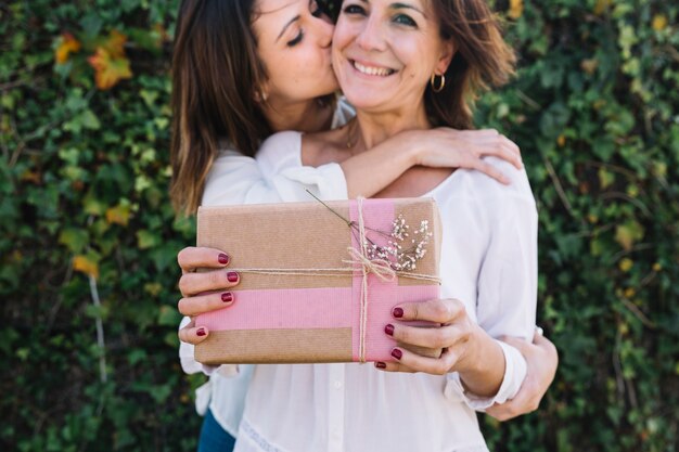 Woman kissing woman with present in cheek