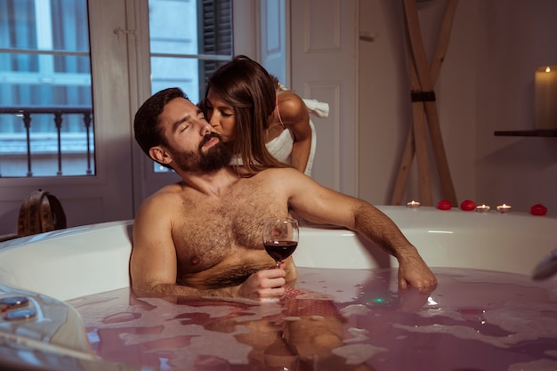 Woman kissing young man with glass of drink in spa tub