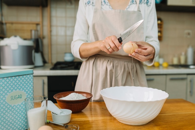 Женщина на кухне разбивает яйцо для приготовления миски