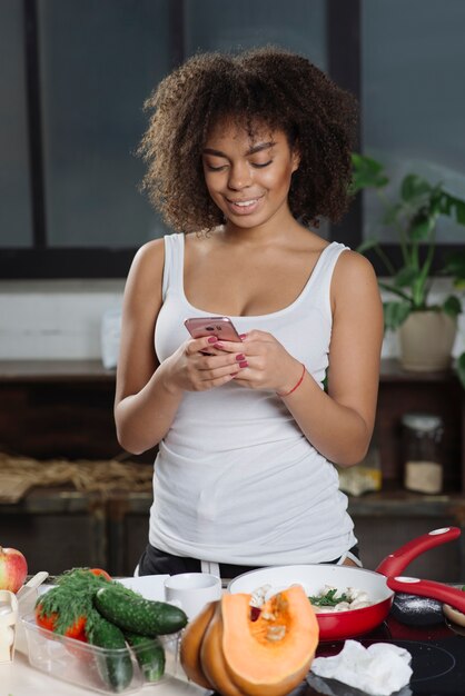 Woman in kitchen typing on smartphone