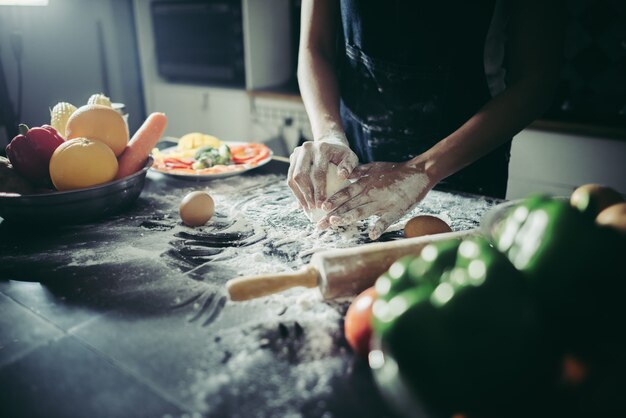 女性は木製の上にピザを作るために生地を混練する。料理のコンセプト。