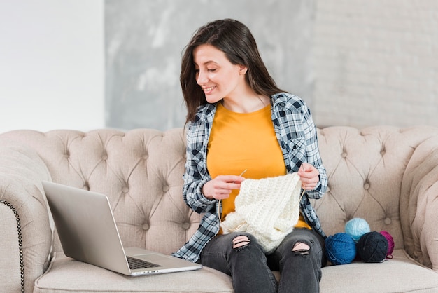 Woman knitting and looking at laptop