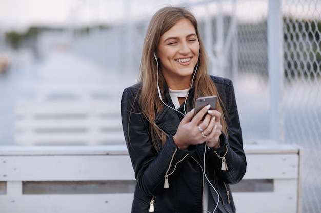 Женщина смеется, слушая музыку держит телефон