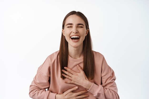 woman laughing and smiling, chuckle from funny joke, amusing tv comedy, touch chest and giggle, standing on white