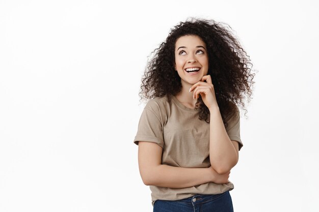 woman laughing, smiling with white teeth and looking happy at upper left corner, standing in t-shirt on white.