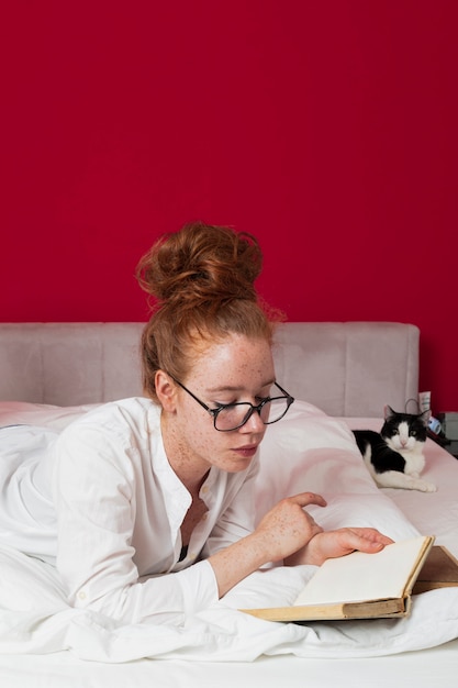 Free photo woman layed on bed with cat reading