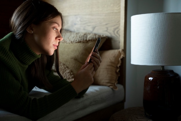 Woman laying on the bed while looking at her smartphone