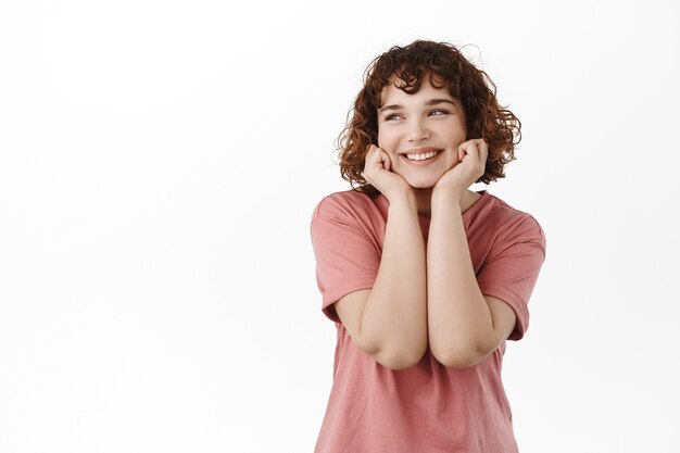 woman, lean face on hands, admire something with dreamy smile standing in t-shirt on white