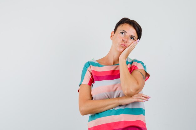 Woman leaning cheek on raised palm in striped t-shirt and looking pensive.