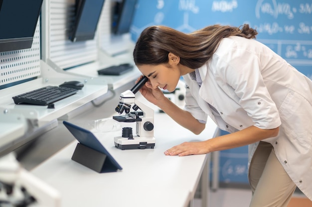 Woman leaning over microscope sideways to camera