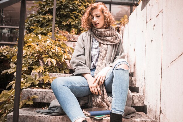 Woman leaning on steps near books 