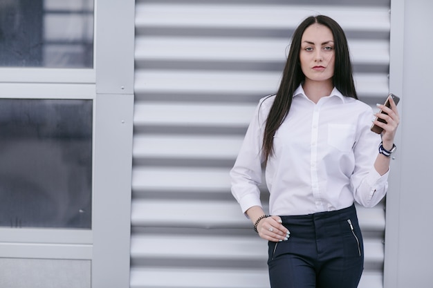 Donna che si appoggia su un muro bianco con un telefono in mano