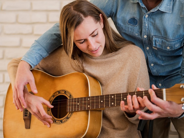 Женщина учится играть на гитаре с учителем дома