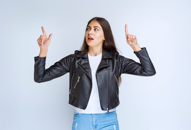 woman in leather jacket pointing at something above.