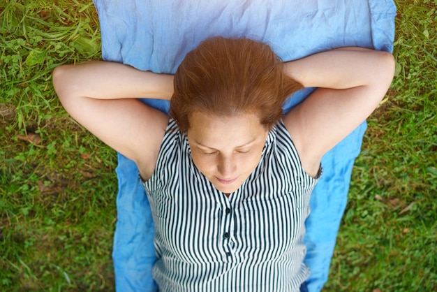 A woman lies on the grass with her eyes closed , relaxed