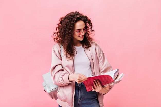 Женщина в легкой одежде читает заметки в блокноте на розовом фоне