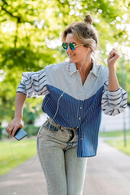 Foto gratuita donna che ascolta la musica e che balla nel parco