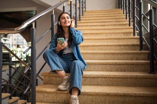 Женщина слушает музыку в наушниках, сидя на лестнице